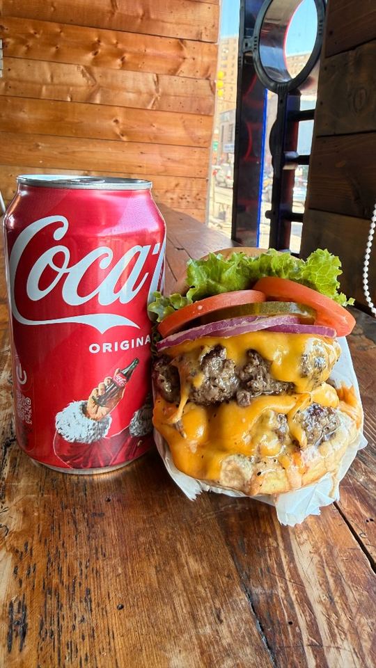 Double cheeseburger and Coke can combo near window seat.
