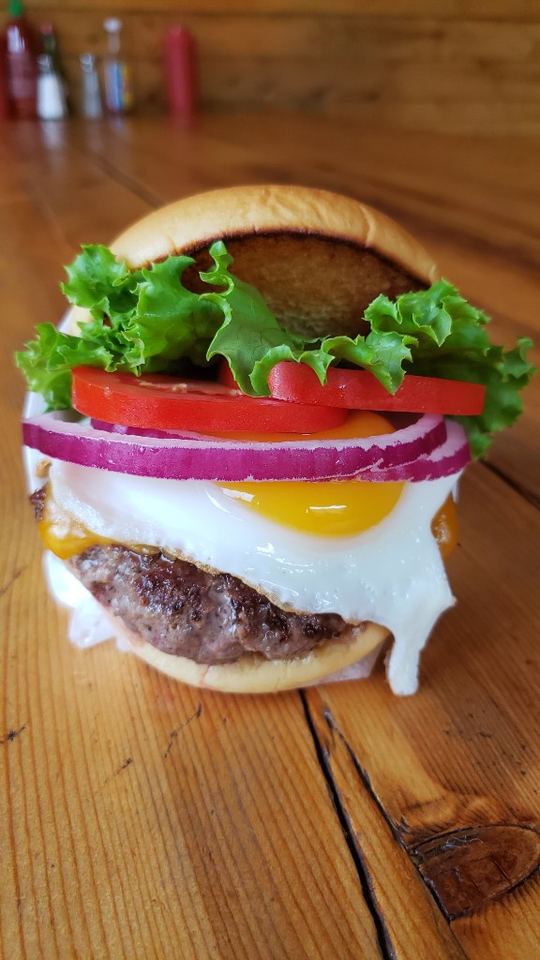 Cheeseburger topped with a runny fried egg, tomato, onion, and lettuce.