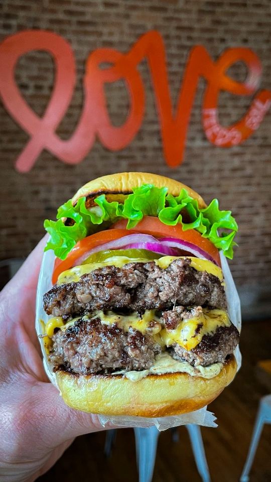 Double cheeseburger held in hand in front of MilkBurger Love wall.