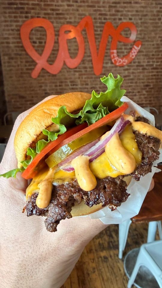 Cheeseburger with house sauce and fresh toppings in front of Love wall.